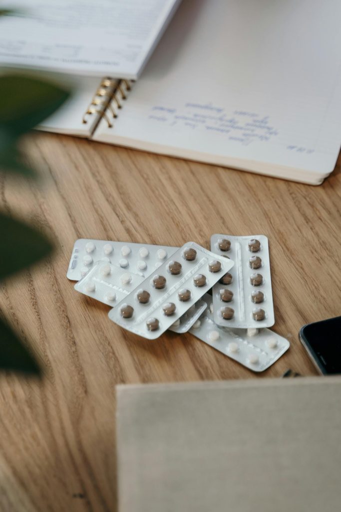 Blister packs with pills on a wooden table alongside an open notebook.