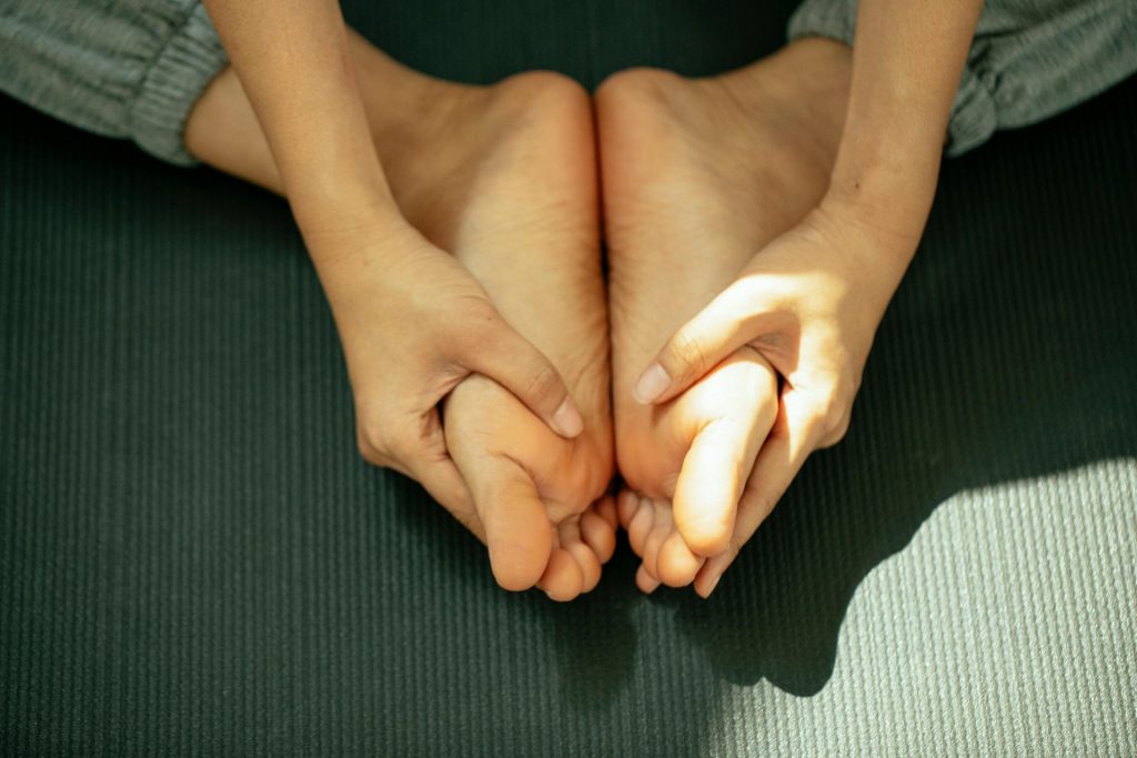 From above of crop anonymous barefooted female in sportswear sitting on mat and practicing Baddha Konasana pose during yoga session